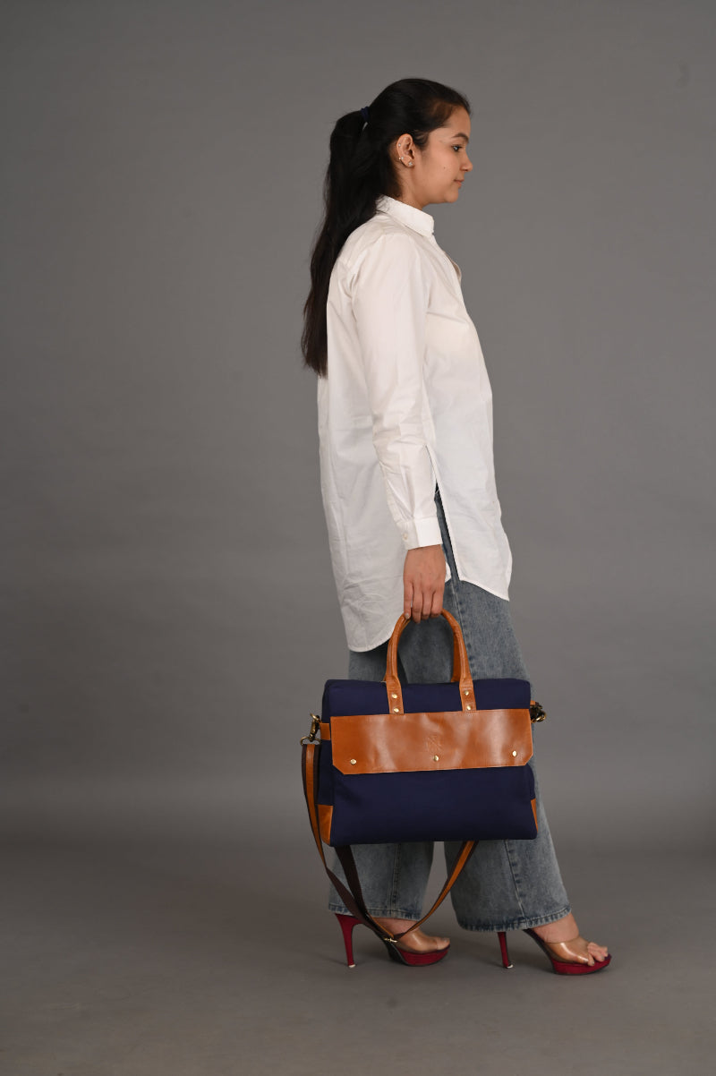 Person holding a navy blue and brown handbag on a gray background