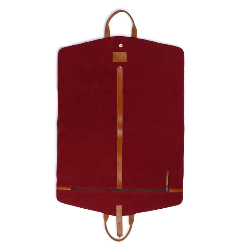 A brown leather garment bag with a soft velvet lining is laid out on a bed, with a person&
