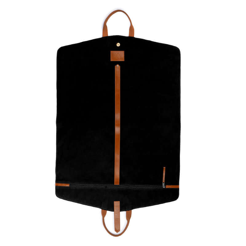 A brown leather garment bag with a soft velvet lining is laid out on a bed, with a person&