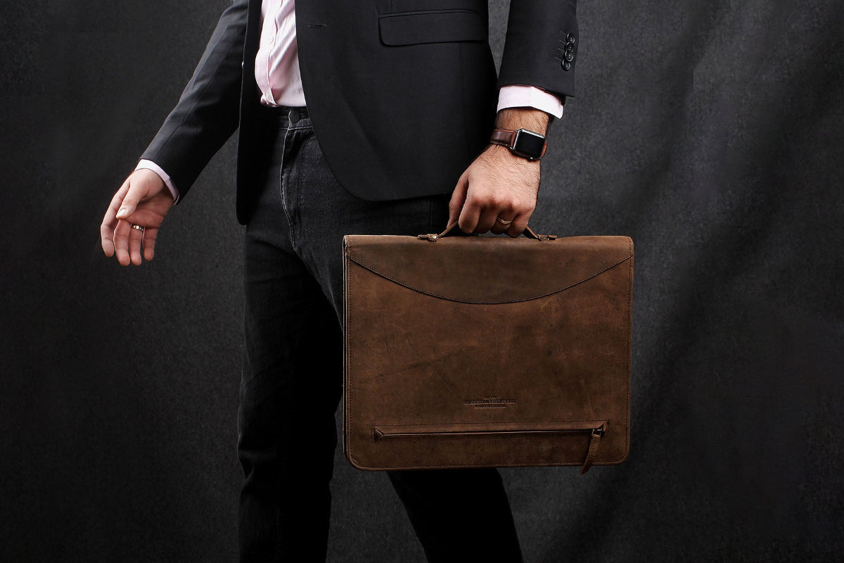 A man in a suit holds a brown briefcase and a file folder, standing confidently in a professional setting.