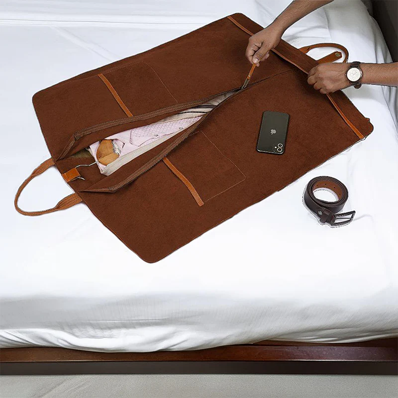 Brown leather travel bag on a bed with items like a phone and belt inside.