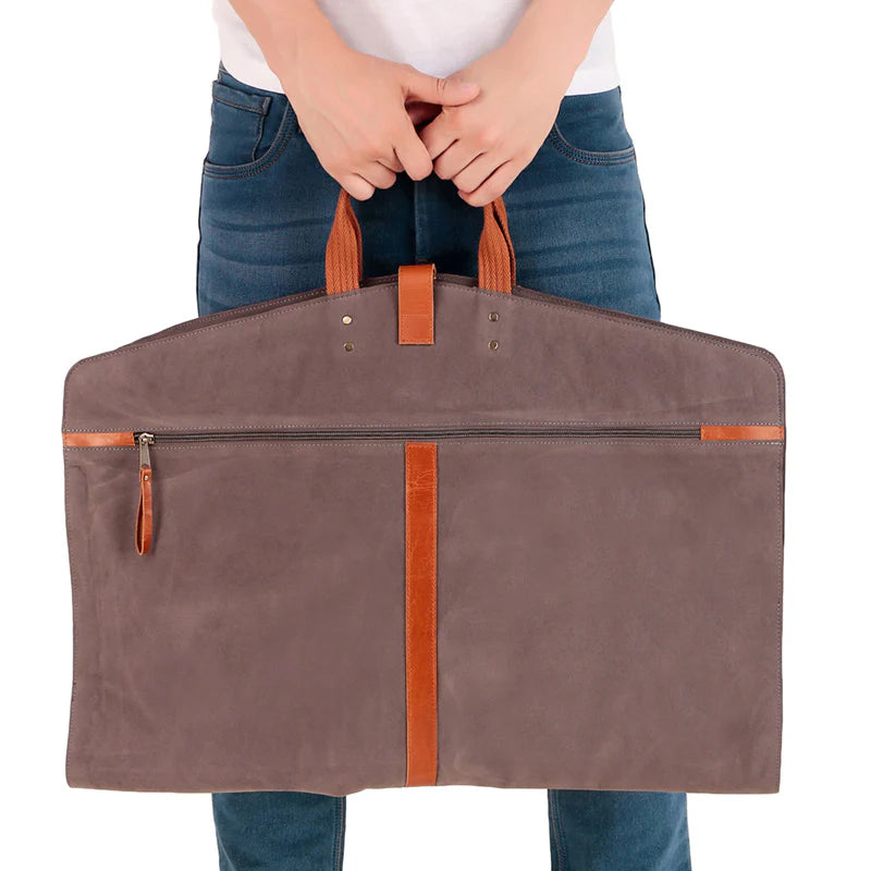 Person holding a brown garment bag with leather handles and trim on a white background