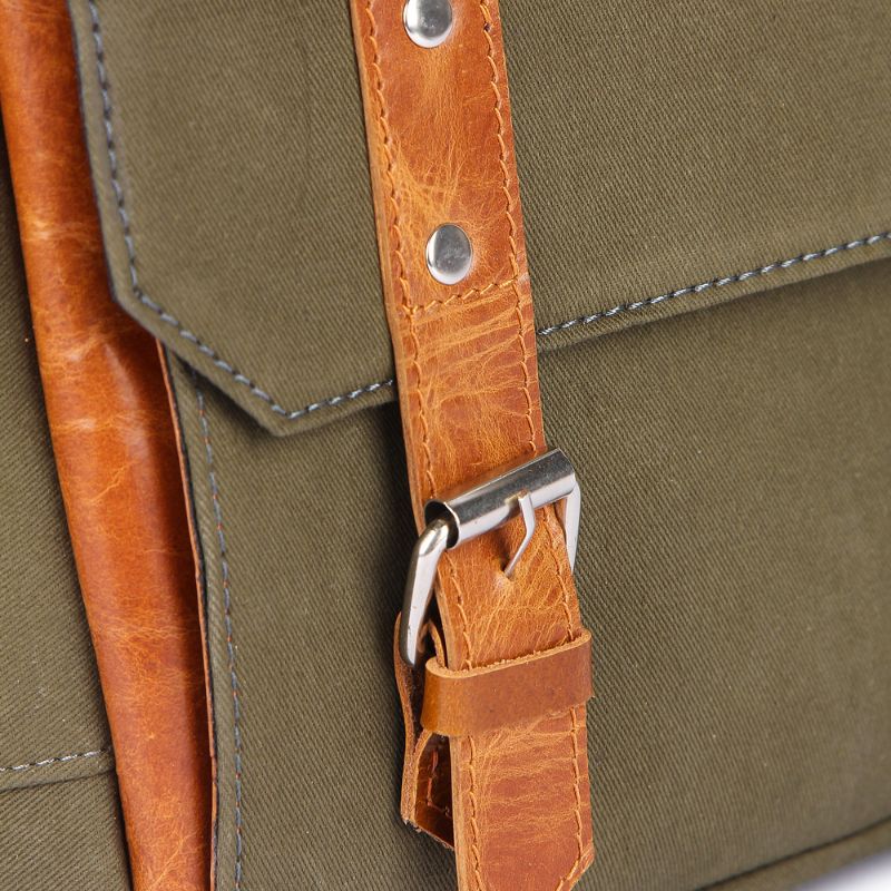 Close-up of a green bag with brown leather straps and buckle.