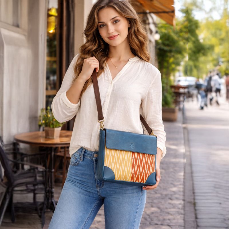 Woman holding a blue crossbody bag with a colorful pattern on a street.
