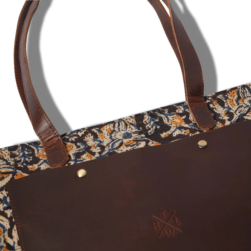 Brown leather tote bag with floral patterned handle on a white background