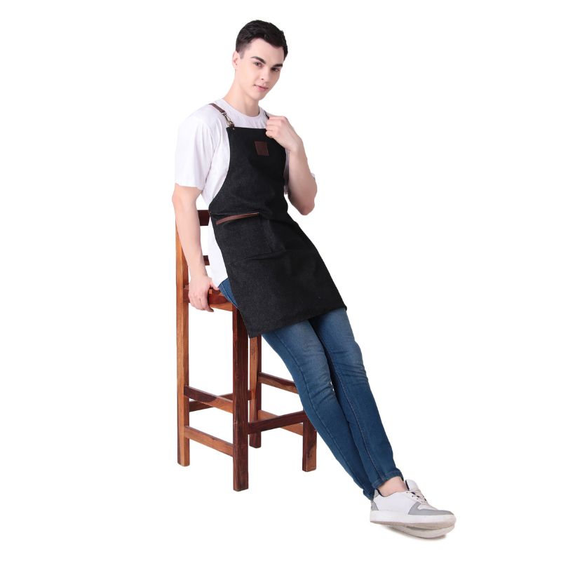 Person wearing a black apron sitting on a wooden stool against a white background