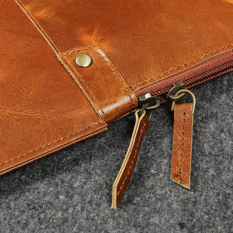 Close-up of a brown leather pouch with a zipper on a gray surface