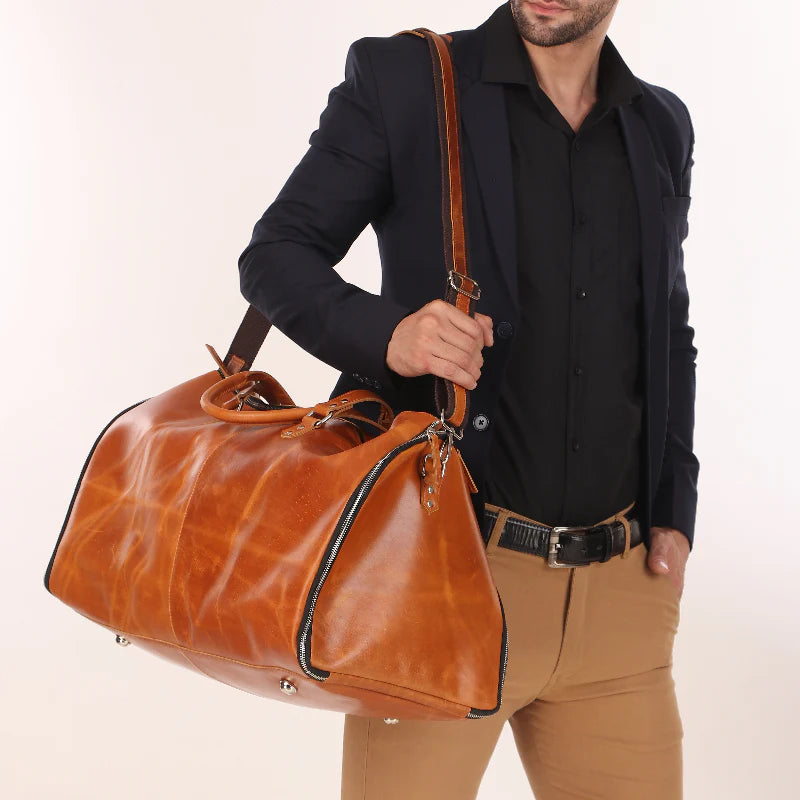 Man holding a brown leather duffel bag against a plain background