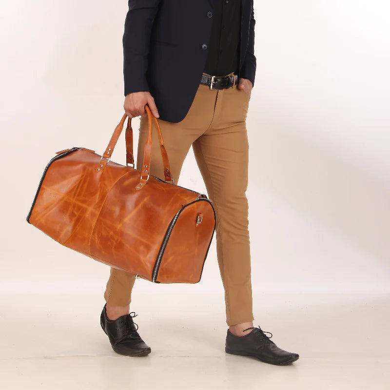 Person holding a brown leather duffel bag against a plain background