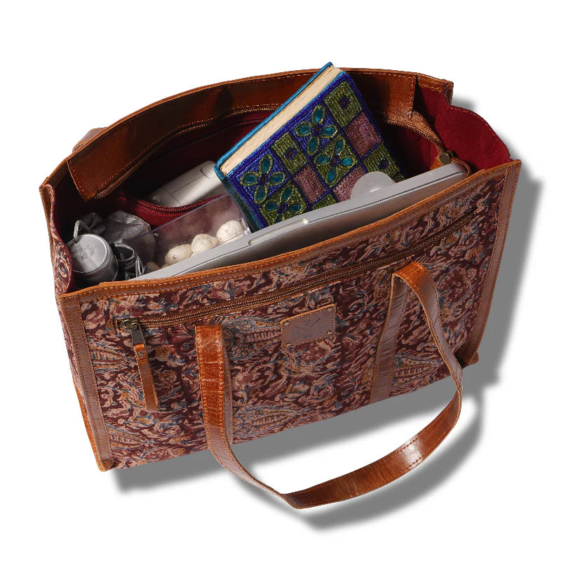 Brown leather handbag with intricate patterns, containing a book and other items on a white background