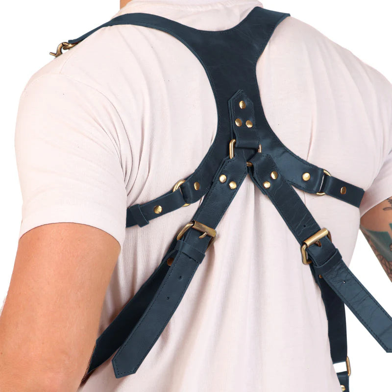 Person wearing a navy leather harness with gold hardware on a white background