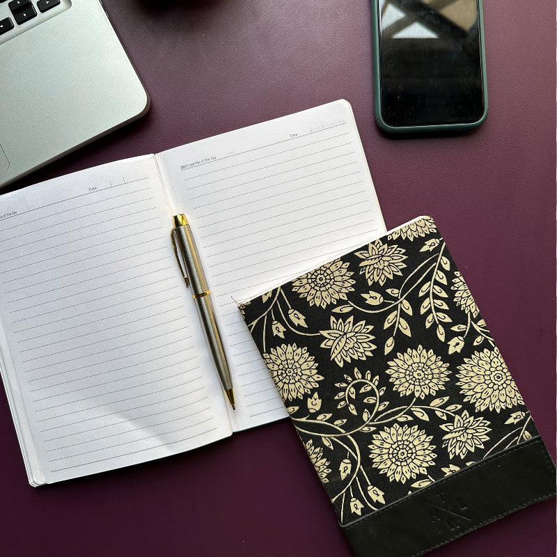 Open notebook with pen, floral-patterned case, and smartphone on a dark surface