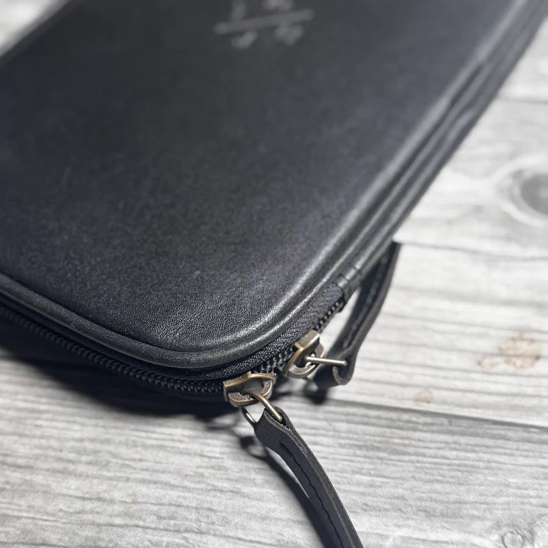 Black leather pouch with gold zipper on a wooden surface