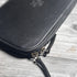 Black leather pouch with gold zipper on a wooden surface