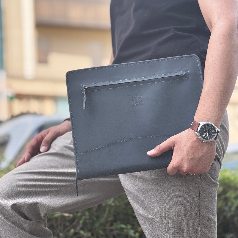 Person holding a dark gray clutch bag outdoors