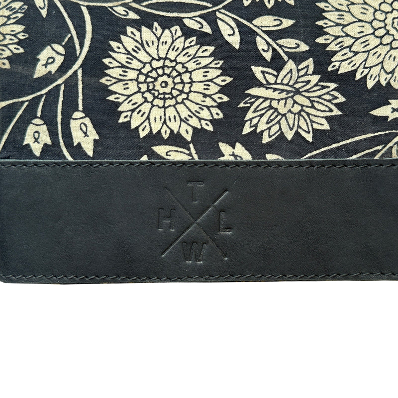 Floral patterned fabric with a leather strip and embossed logo on a white background