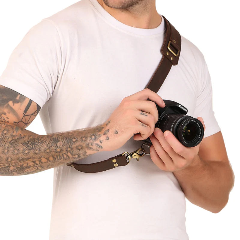 Person holding a camera with a brown leather strap on a white background