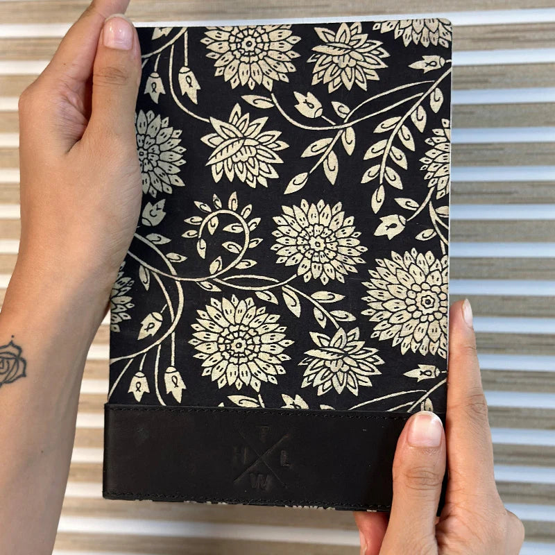 Hand holding a black notebook with white floral pattern against a striped background