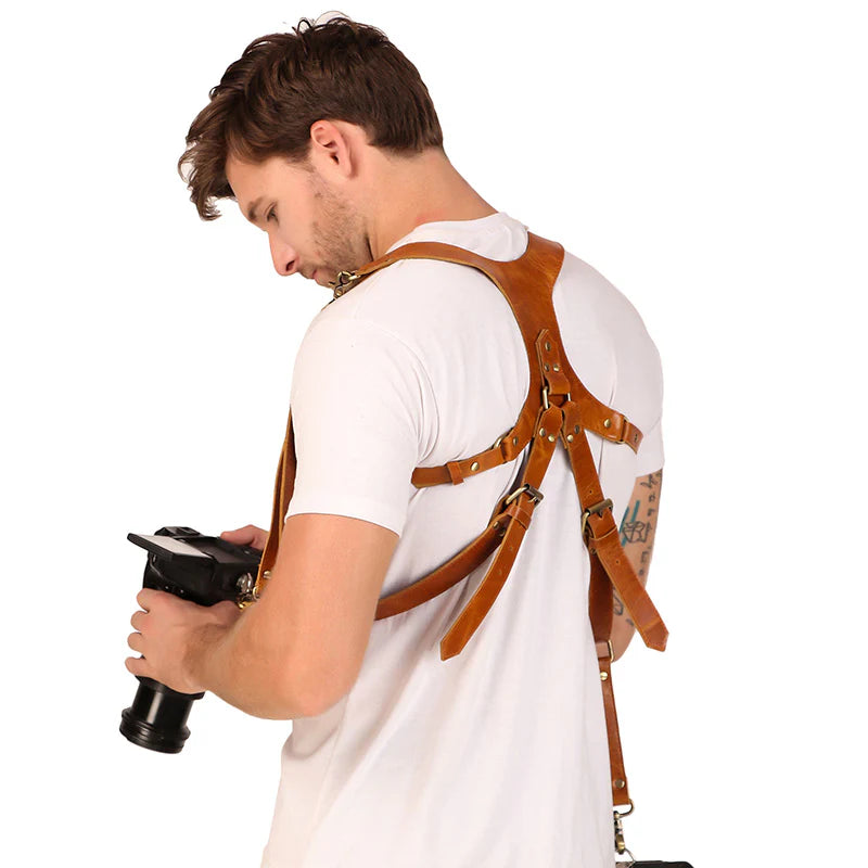 Man wearing a brown leather harness holding a camera on a white background