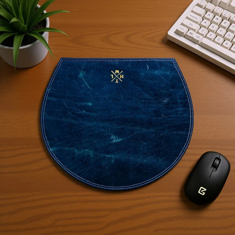 Blue mouse pad on a wooden desk with a plant and keyboard in the background