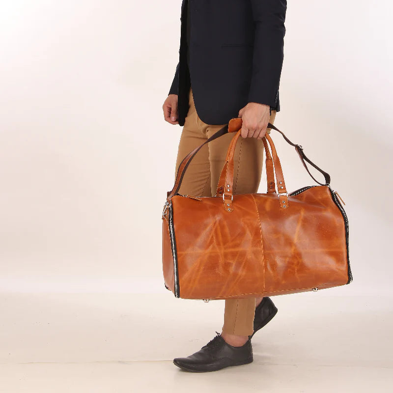 Person holding a brown leather duffel bag against a plain background