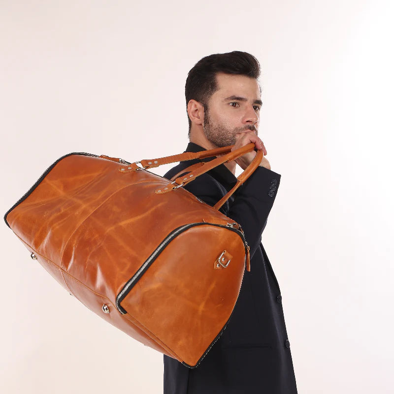 Man holding a brown leather duffel bag against a plain background