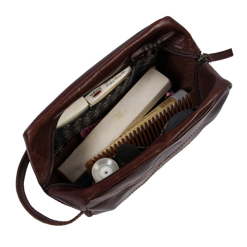 Brown leather toiletry bag with grooming products on a white background