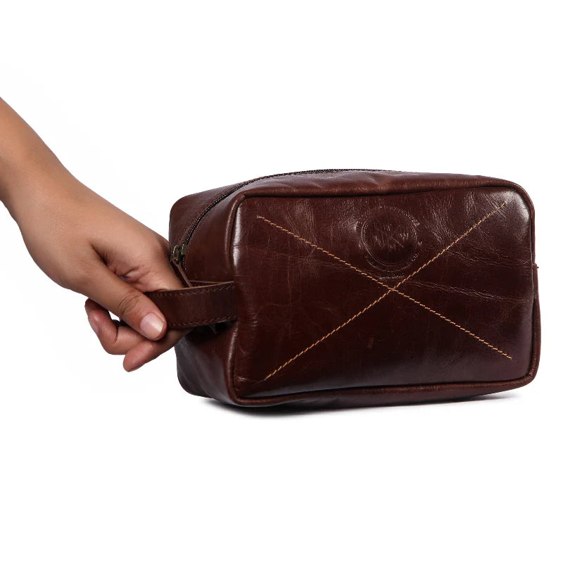 Brown leather toiletry bag held by a hand on a white background