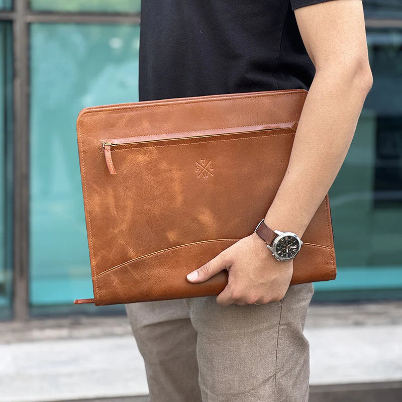 Person holding a brown leather clutch bag with a blurred background
