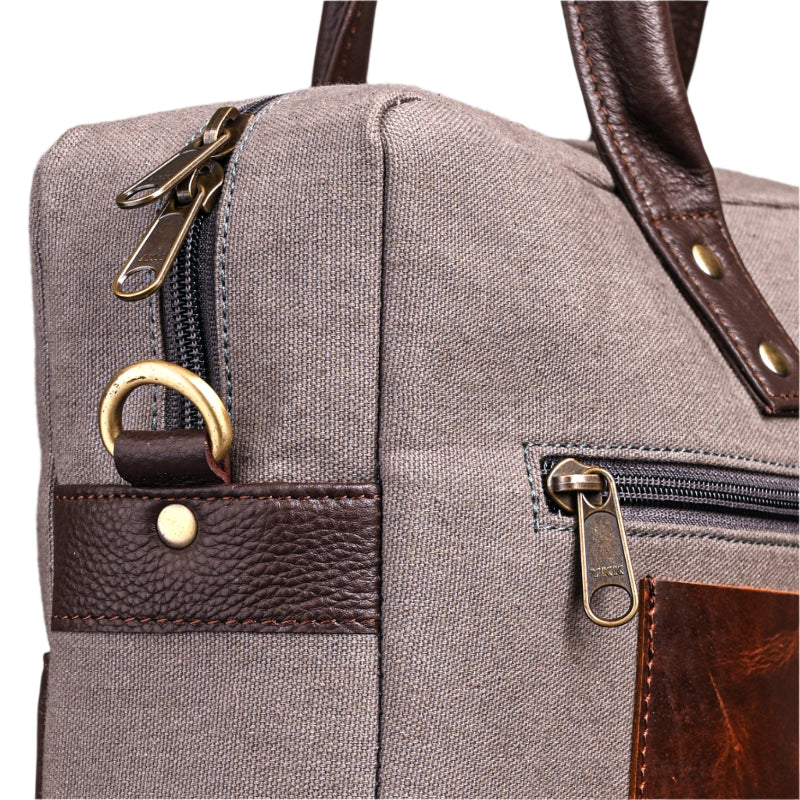 Close-up of a gray bag with brown leather accents and gold zippers.