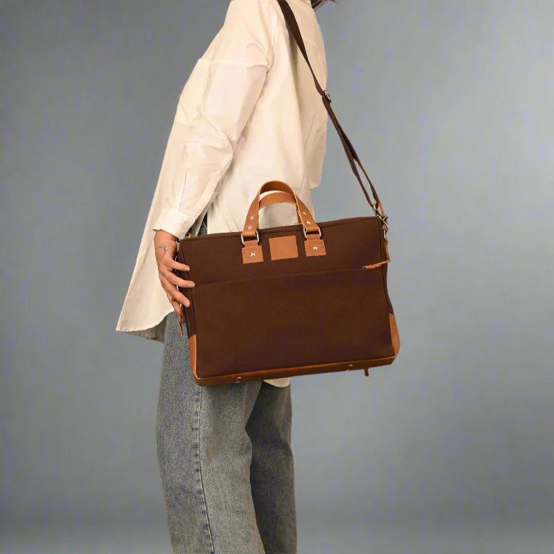 Person holding a brown leather briefcase against a gray background