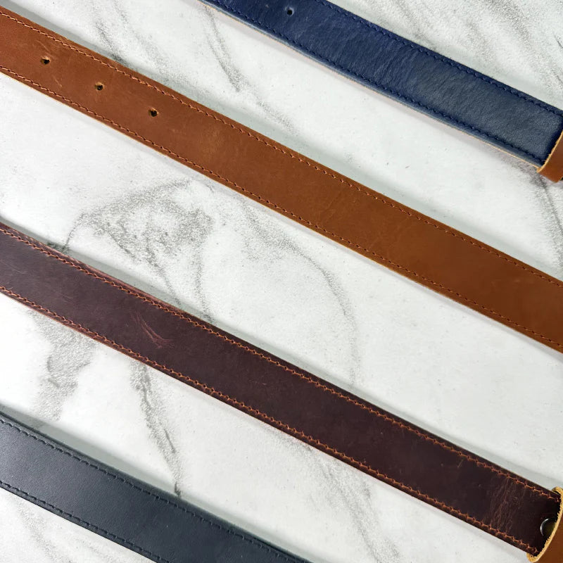 Four leather belts in brown, blue, and black on a marble surface