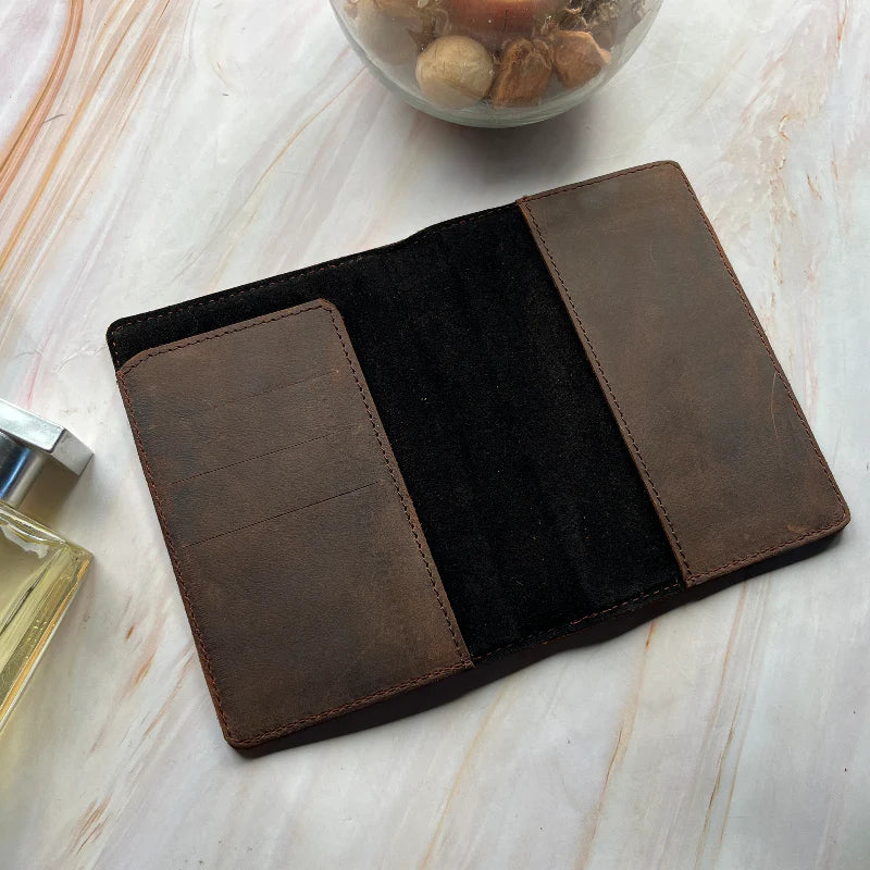 Brown leather wallet on a light wooden surface with a glass container of stones in the background.