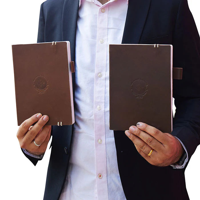 Person holding two brown leather notebooks with a visible brand logo.