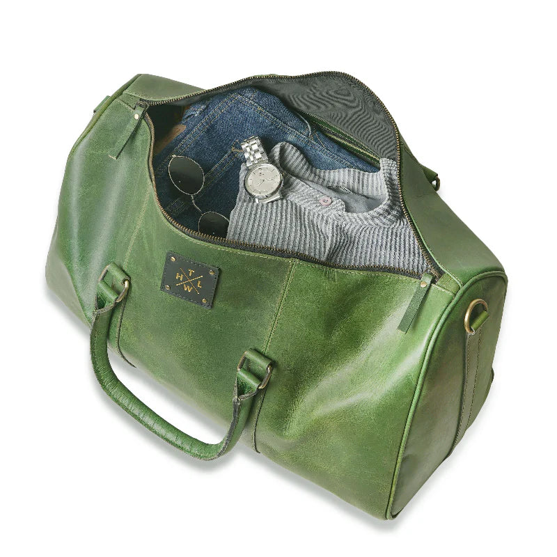 Green leather duffel bag with clothing and accessories on a white background