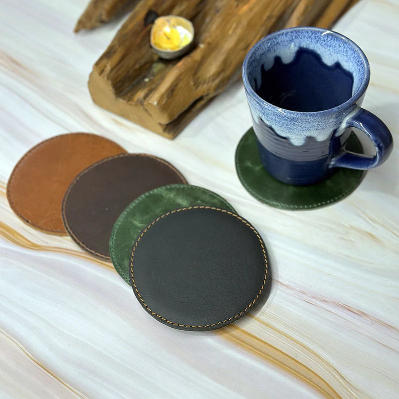 Set of leather coasters in different colors on a marble surface with a mug.