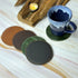 Set of leather coasters in different colors on a marble surface with a mug.