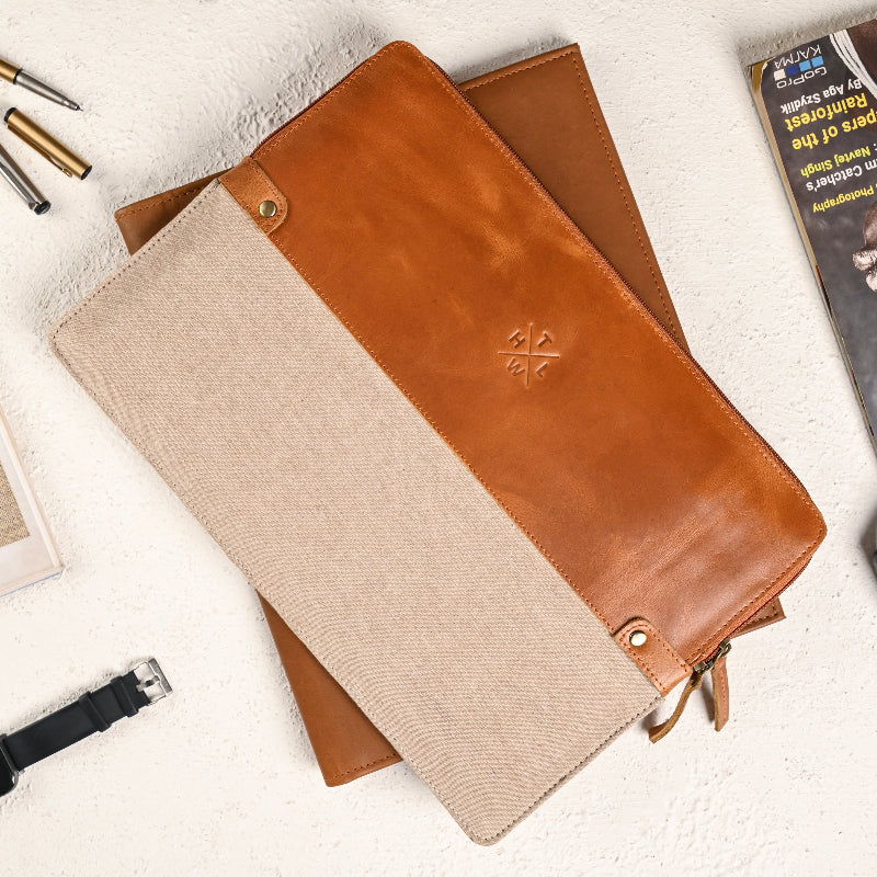 Brown leather and beige fabric wallet on a light surface with stationery items.