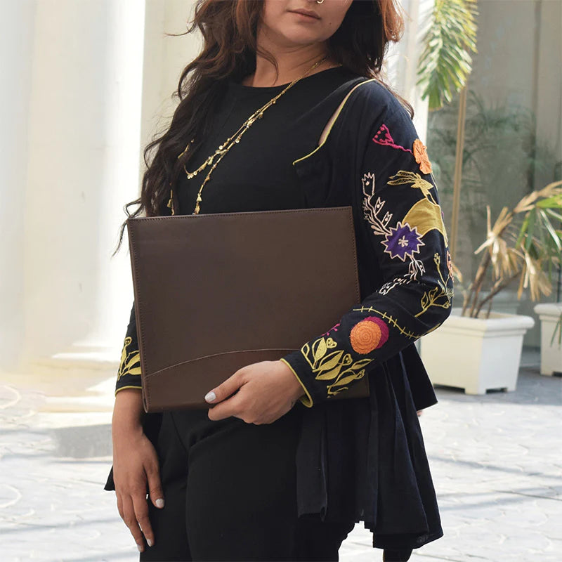 Woman holding a brown clutch with floral embroidery in an outdoor setting