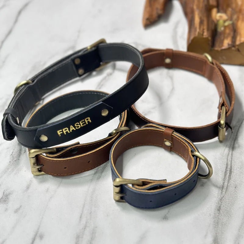Three leather dog collars in black, brown, and blue on a marble surface with &