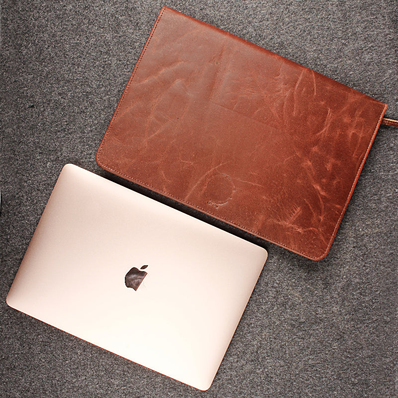 Brown leather sleeve on a silver laptop with Apple logo on a gray surface