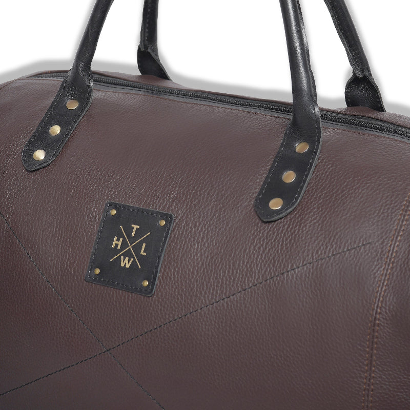 Brown leather bag with black handles and a logo on a white background