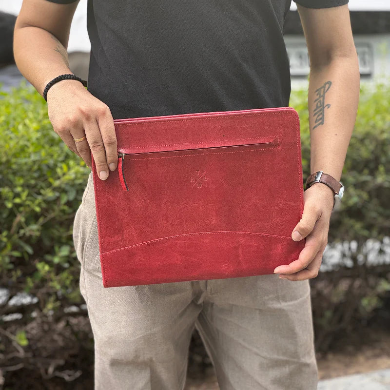 Person holding a red clutch bag outdoors with greenery in the background