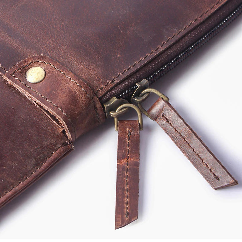 Close-up of a brown leather bag with a zipper and decorative tag on a white background
