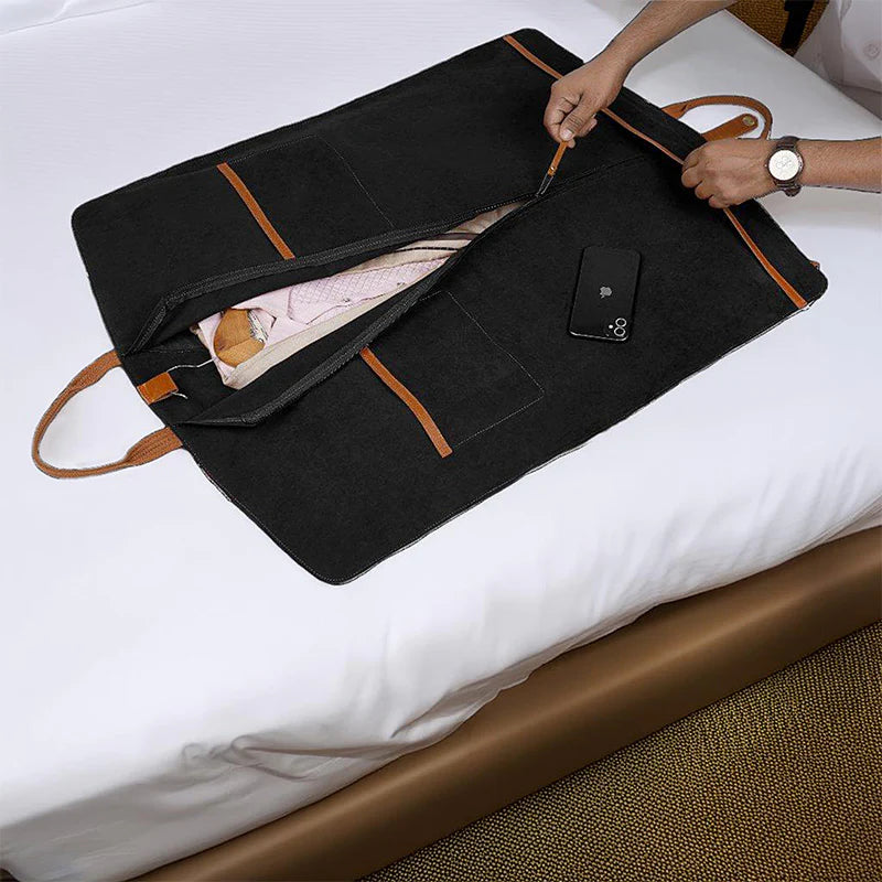 Black garment bag with brown straps on a bed