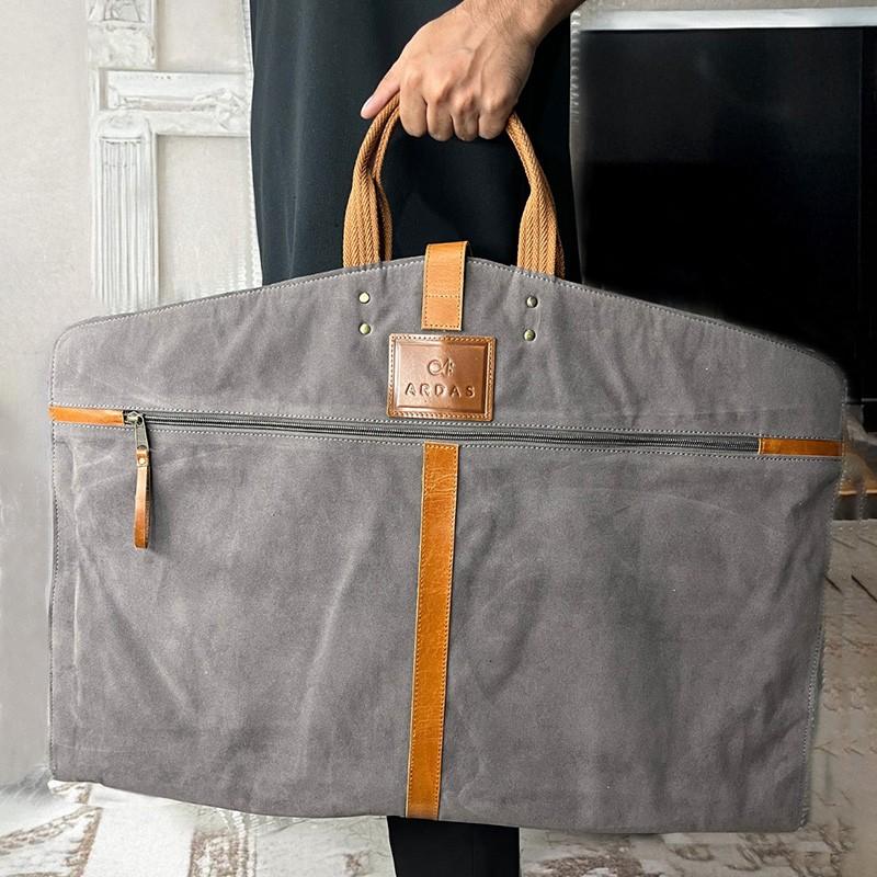 Gray garmen bag with brown accents held by a person indoors