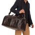 Man holding a brown leather duffel bag against a white background