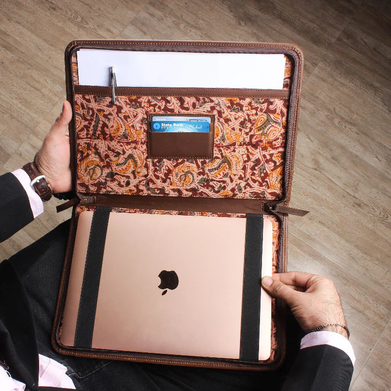Person holding a laptop in a brown paisley-patterned case on a wooden floor.