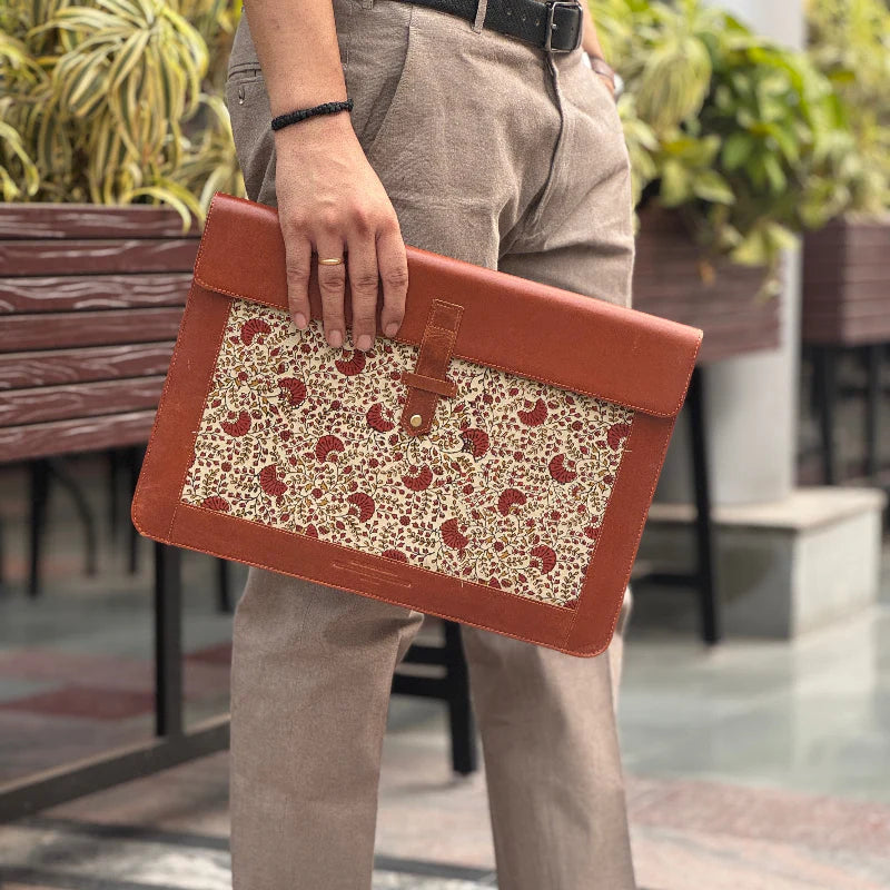 Person holding a brown leather clutch with floral pattern outdoors