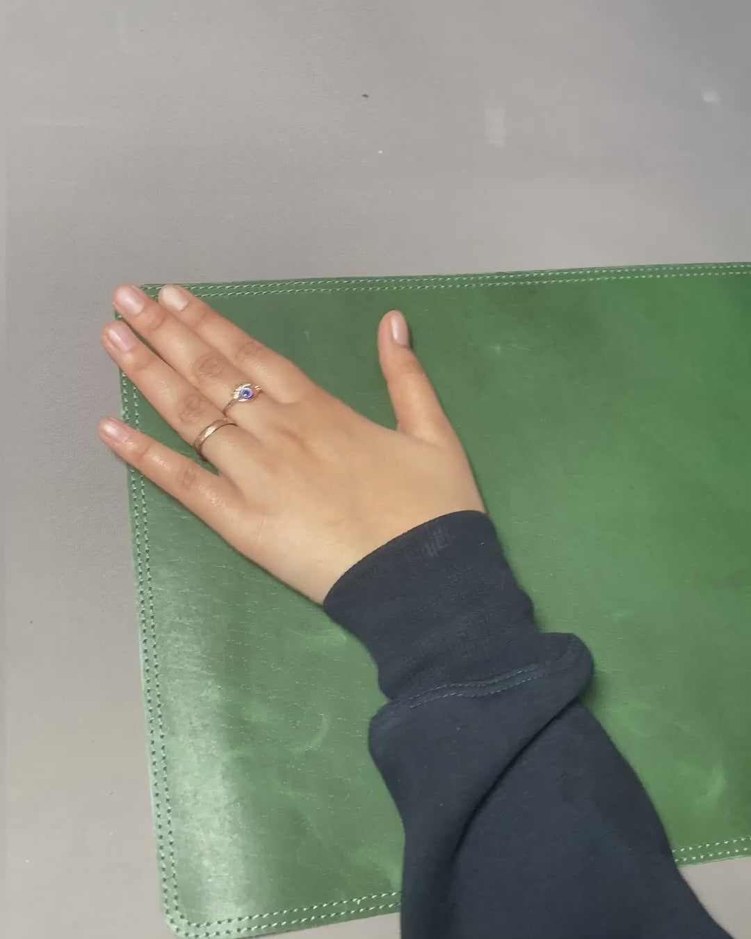 A person holding a green leather wallet labeled "genuine leather" on a desk mat.